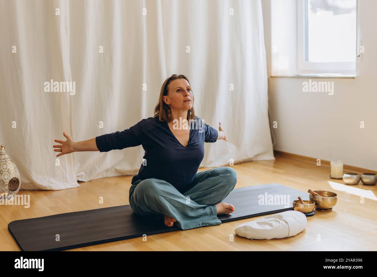 Una donna siede sul pavimento con gli occhi chiusi, praticando esercizi di respirazione profonda. Lei inala ed espira lentamente. Foto di alta qualità Foto Stock