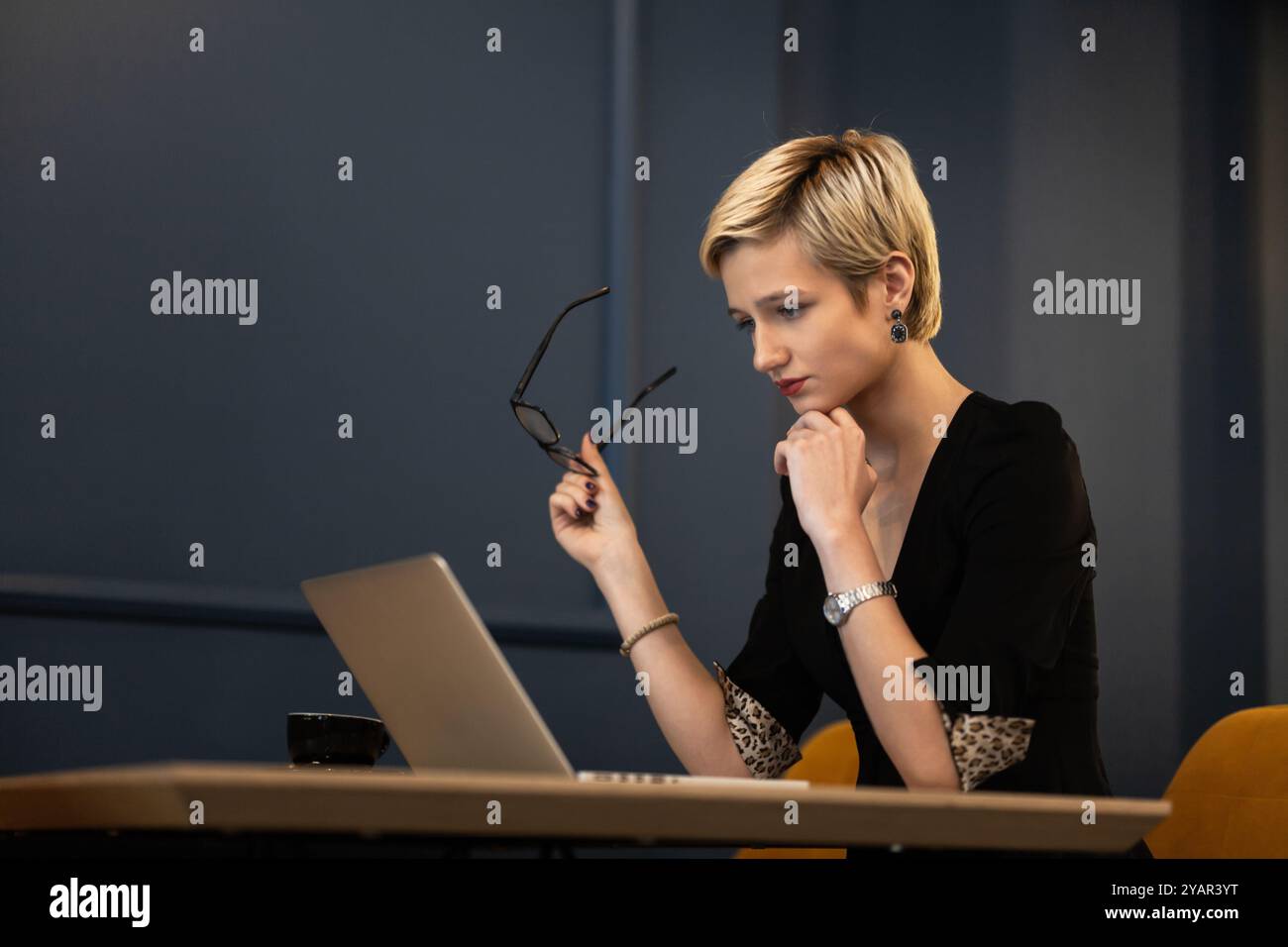 Una giovane donna con un taglio pixie è profondamente impegnata con il suo lavoro su un notebook a una scrivania in un ambiente di ufficio elegante, dimostrando professionalità e Foto Stock