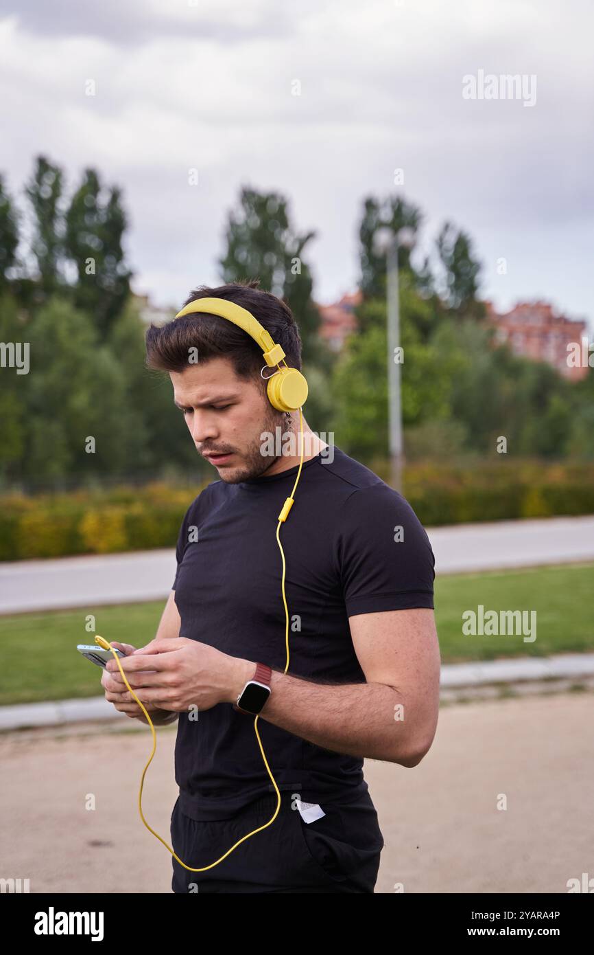 giovane uomo attraente che cammina mentre ascolta la musica con le cuffie tramite il suo smartphone. fotografia verticale. Foto Stock
