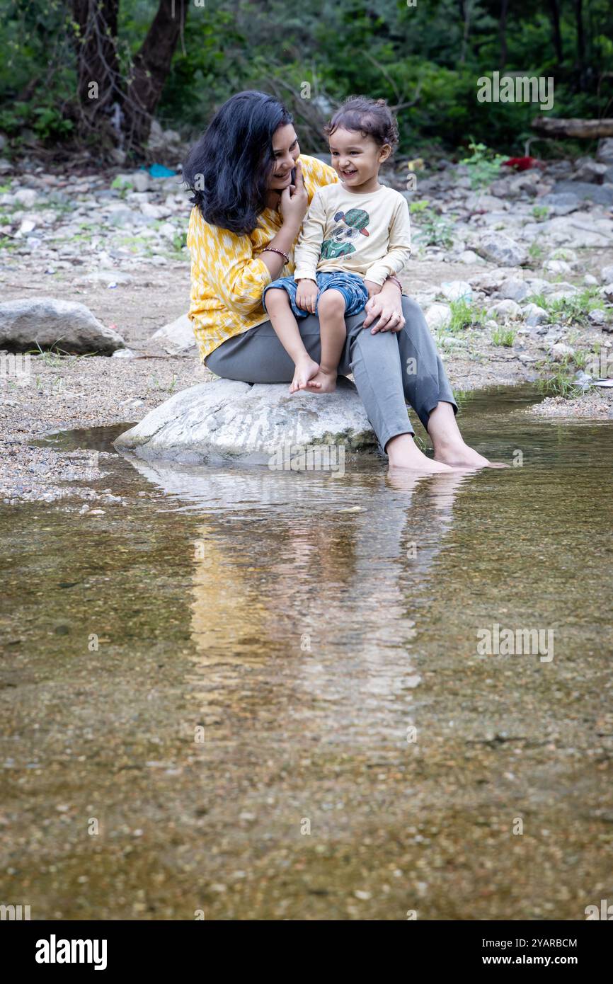 Donna isolata che passa del tempo con il figlio sulla pietra al Calm Lake Shore al mattino Foto Stock