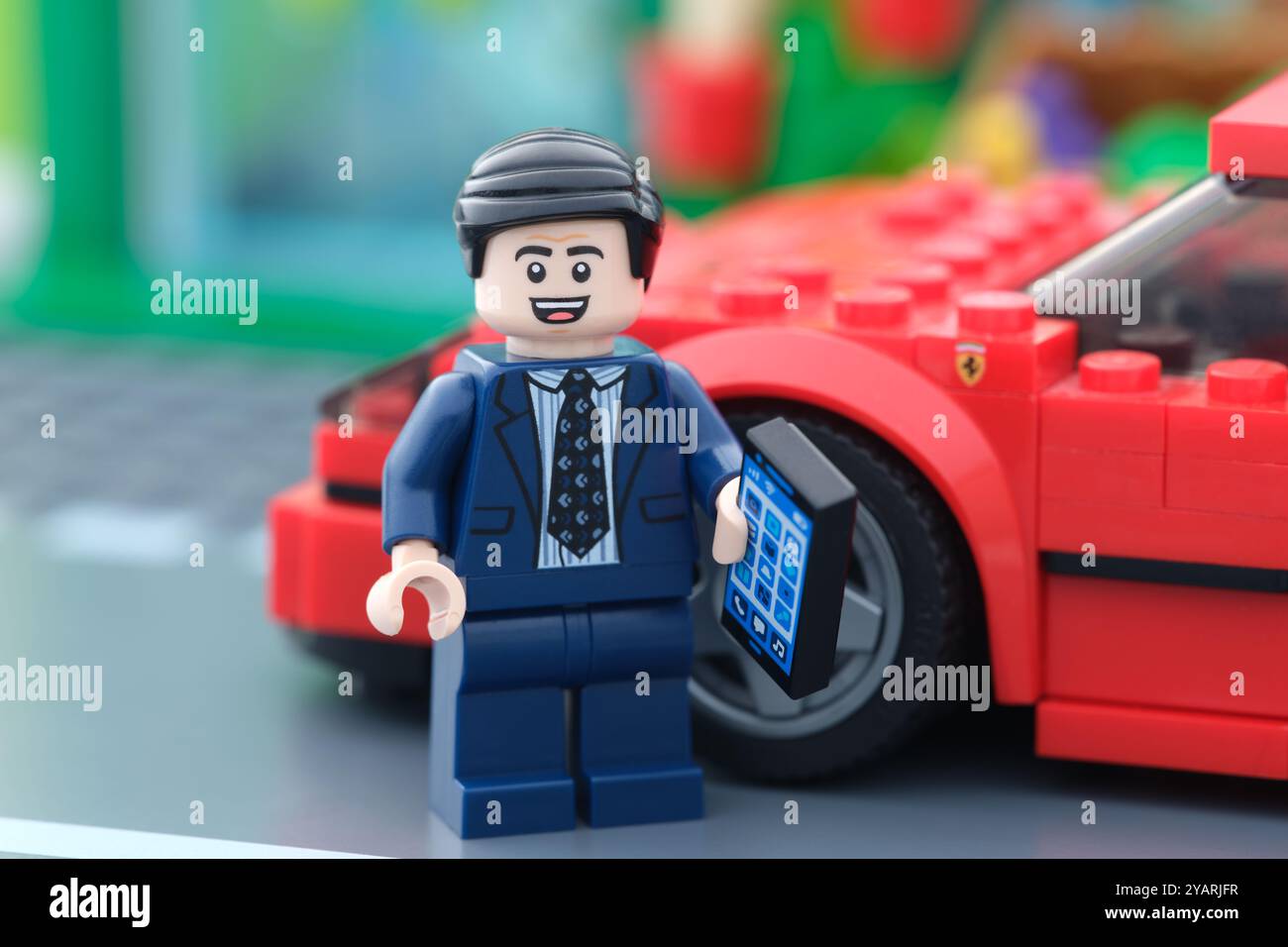 Tambov, Federazione Russa - 15 ottobre 2024 Una minifigura d'affari Lego in piedi di fronte alla sua auto Lego Ferrari F40 e con in mano un cellulare. Foto Stock
