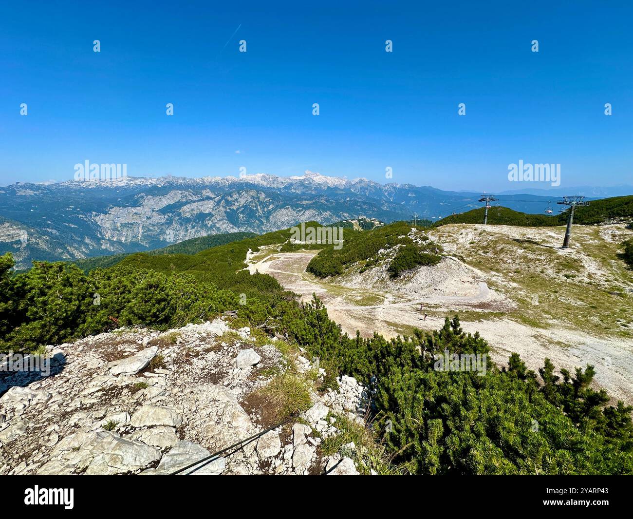 Una fotografia cattura un paesaggio montano soleggiato mozzafiato in una limpida giornata estiva, con lussureggianti colline verdi e vette torreggianti. Foto Stock