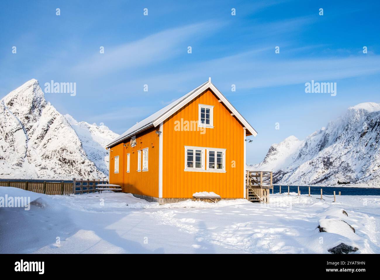 Tradizionale casa di rorbu gialla e vetta della montagna Olstind nel villaggio di pescatori di Sakrisoy sulle isole Lofoten, Norvegia. Paesaggio invernale con montagne innevate Foto Stock
