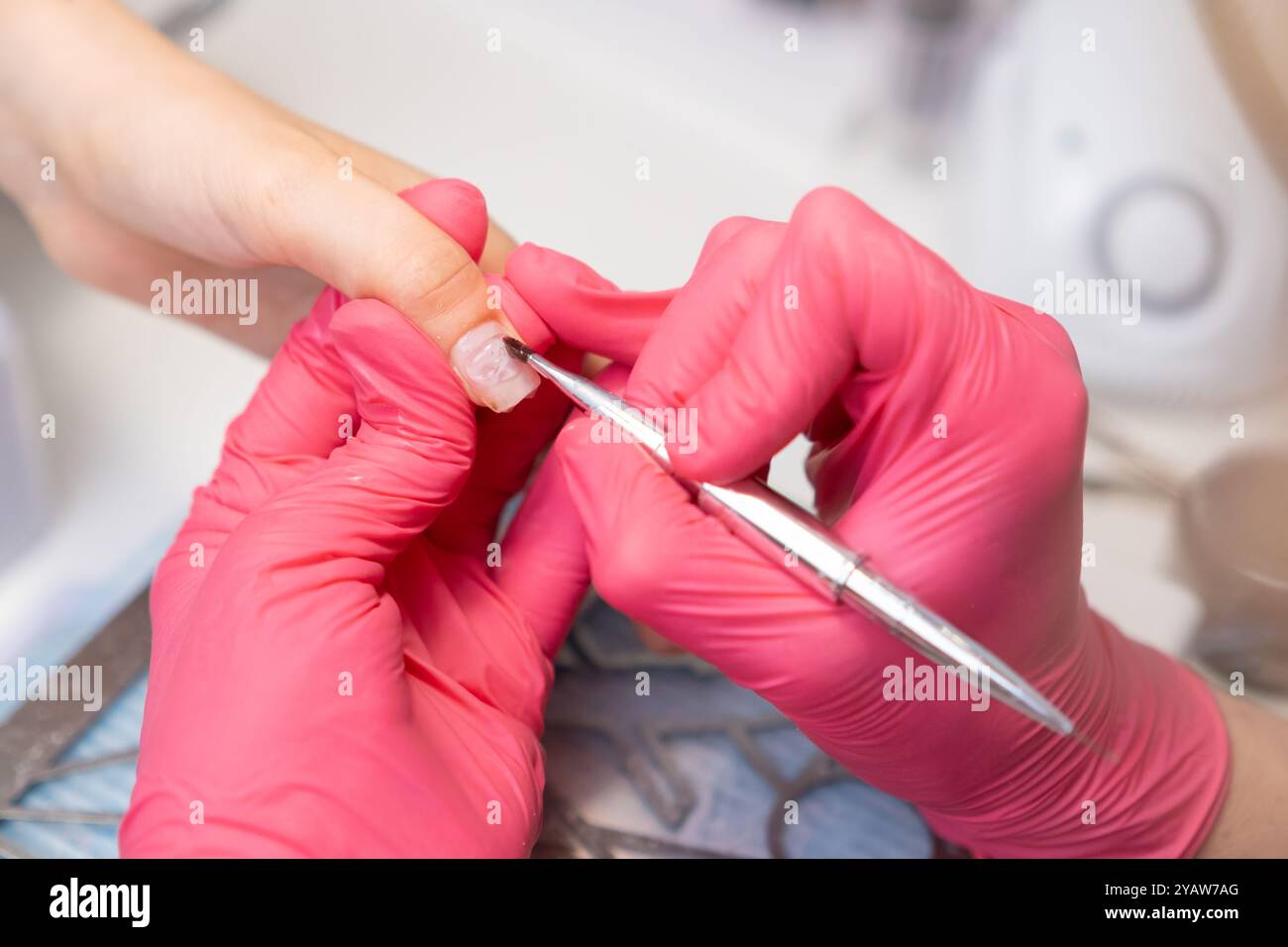 Il manicurista applica uno strato base di smalto gel sull'unghia della donna utilizzando una spazzola nel salone di bellezza. Foto Stock