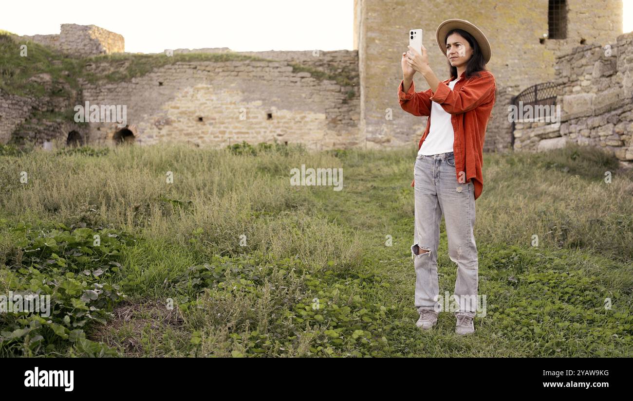 Donna turistica che scatta foto di un'antica fortezza per un blog di viaggio. Ama documentare i monumenti storici e condividere la sua esperienza di viaggio Foto Stock