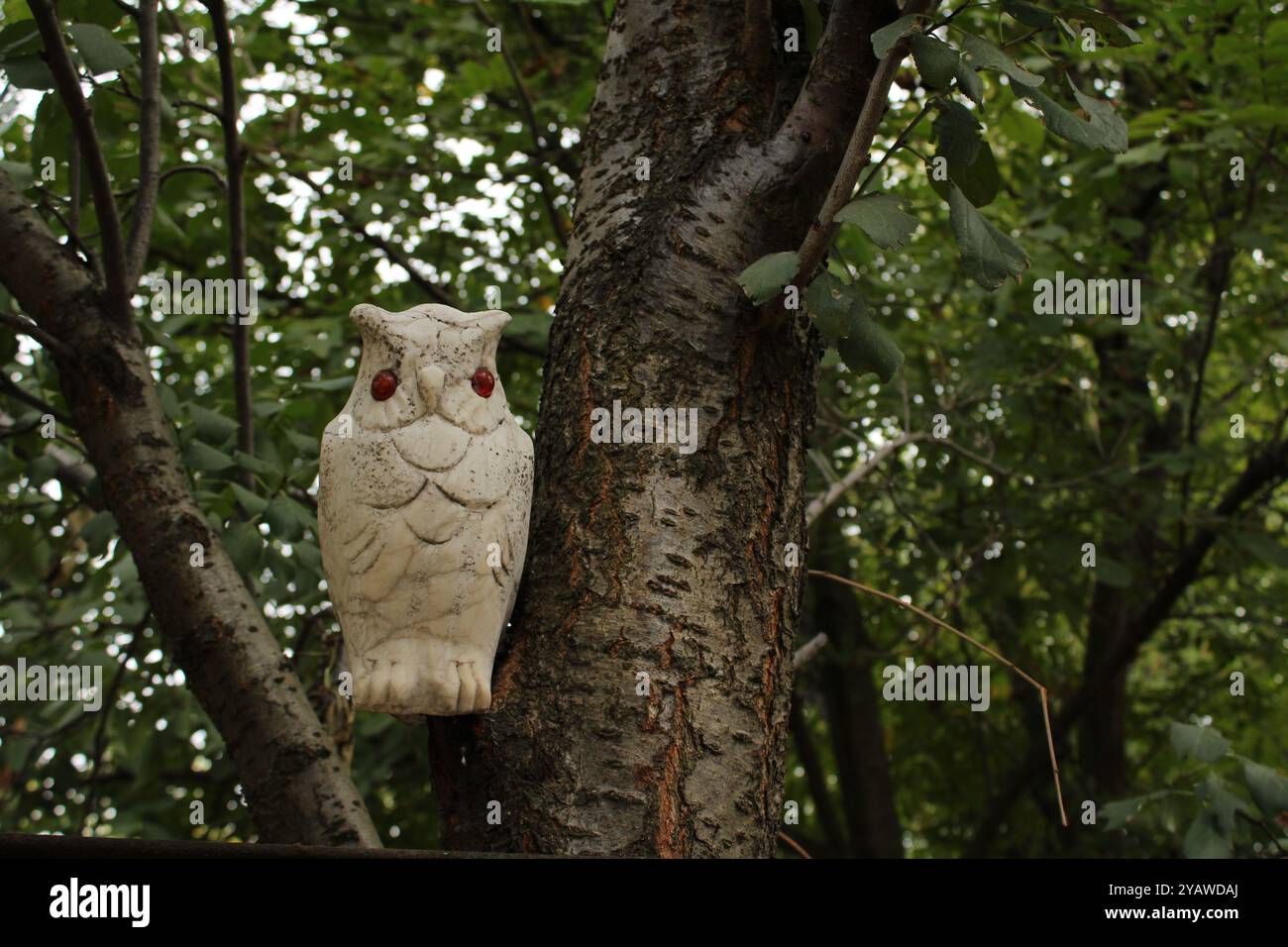Il gufo di ceramica sull'albero sembra una parte della natura, mescolandosi perfettamente con i rami e le foglie. Foto Stock