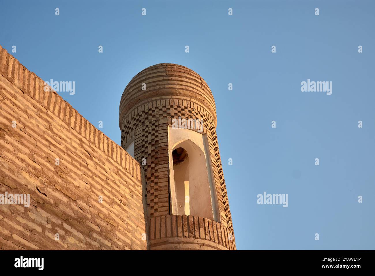 Questo antico minareto, alto accanto a un vecchio edificio nella storica città di Khiva, Uzbekistan, è un simbolo notevole del ricco culto della regione Foto Stock