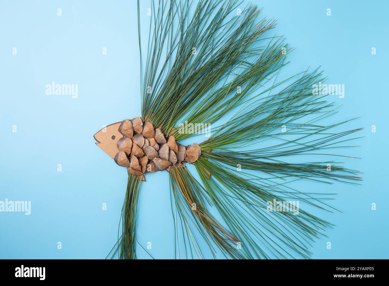 Forma di pesce composta da coni di pino e aghi di pino su sfondo blu. Composizione piatta. Concetto artistico ispirato alla natura. Design per poster e biglietti d'auguri Foto Stock