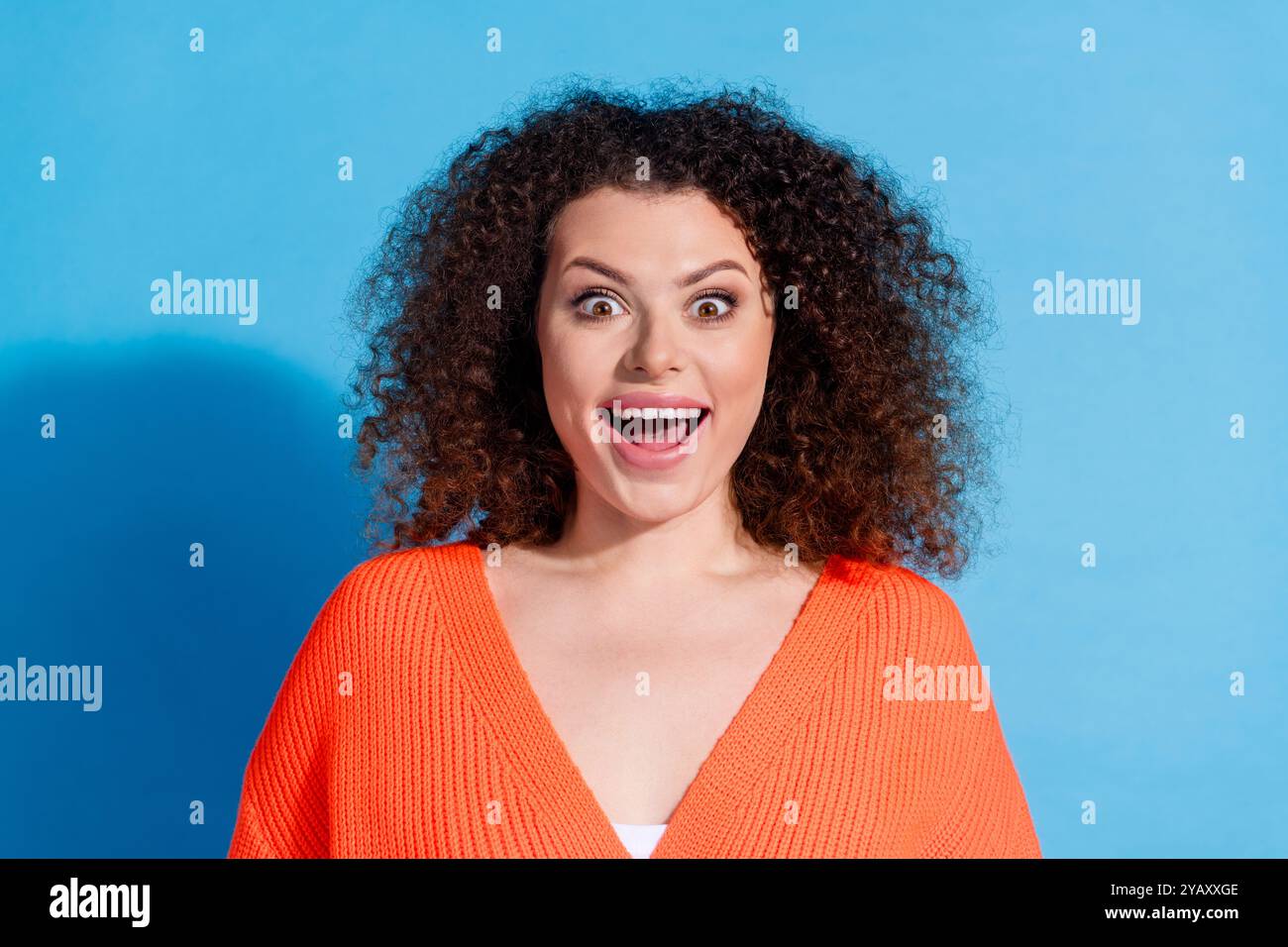 Foto ritratto di capelli ondulati scioccata guardando video donna latina  che indossa un cardigan arancione isolato su sfondo blu Foto stock - Alamy