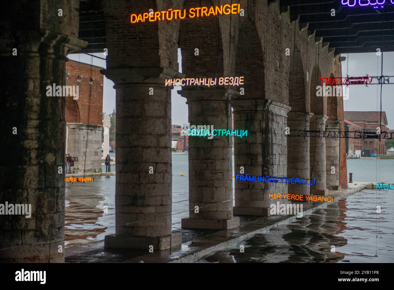 Venezia 8 ottobre 2024: Biennale Internazionale d'Arte di Venezia luci a LED colorate che riflettono le parole che siamo tutti stranieri nell'acqua Foto Stock