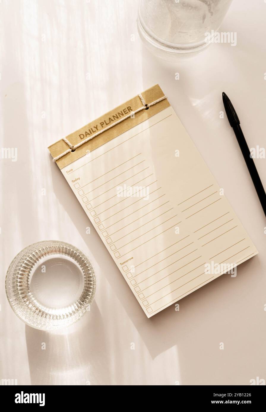Pianificatore quotidiano minimalista piatto dal design semplice, con caselle di controllo e linee per le attività. Superficie leggera accanto a una tazza di vetro, per una pulizia ottimale Foto Stock