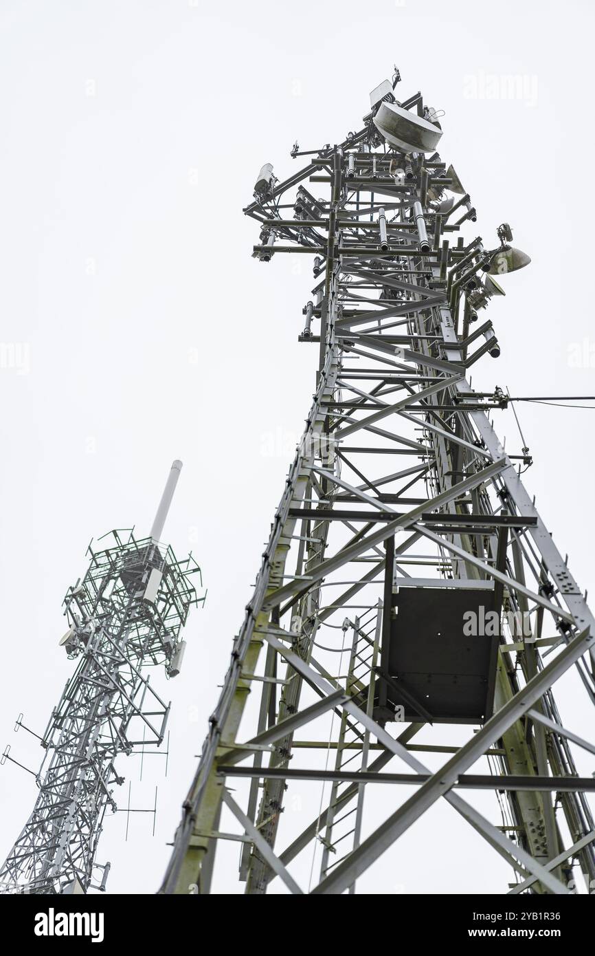 Vista da terra verso l'alto di due grandi montanti per telefoni cellulari con molti piatti per telecomunicazioni. Foto Stock