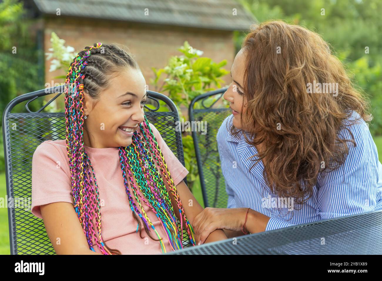 Madre e figlia stanno parlando insieme seduti al tavolo del giardino. Orizzontalmente. Foto Stock