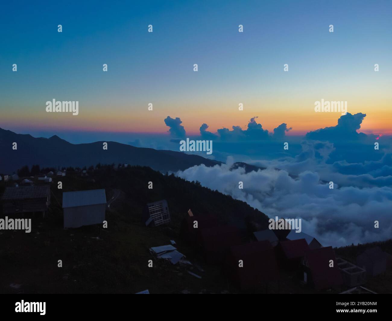 Tramonto colorato che illumina un mare di nuvole che copre una valle di montagna, con un piccolo villaggio che inizia a emergere dalla nebbia Foto Stock