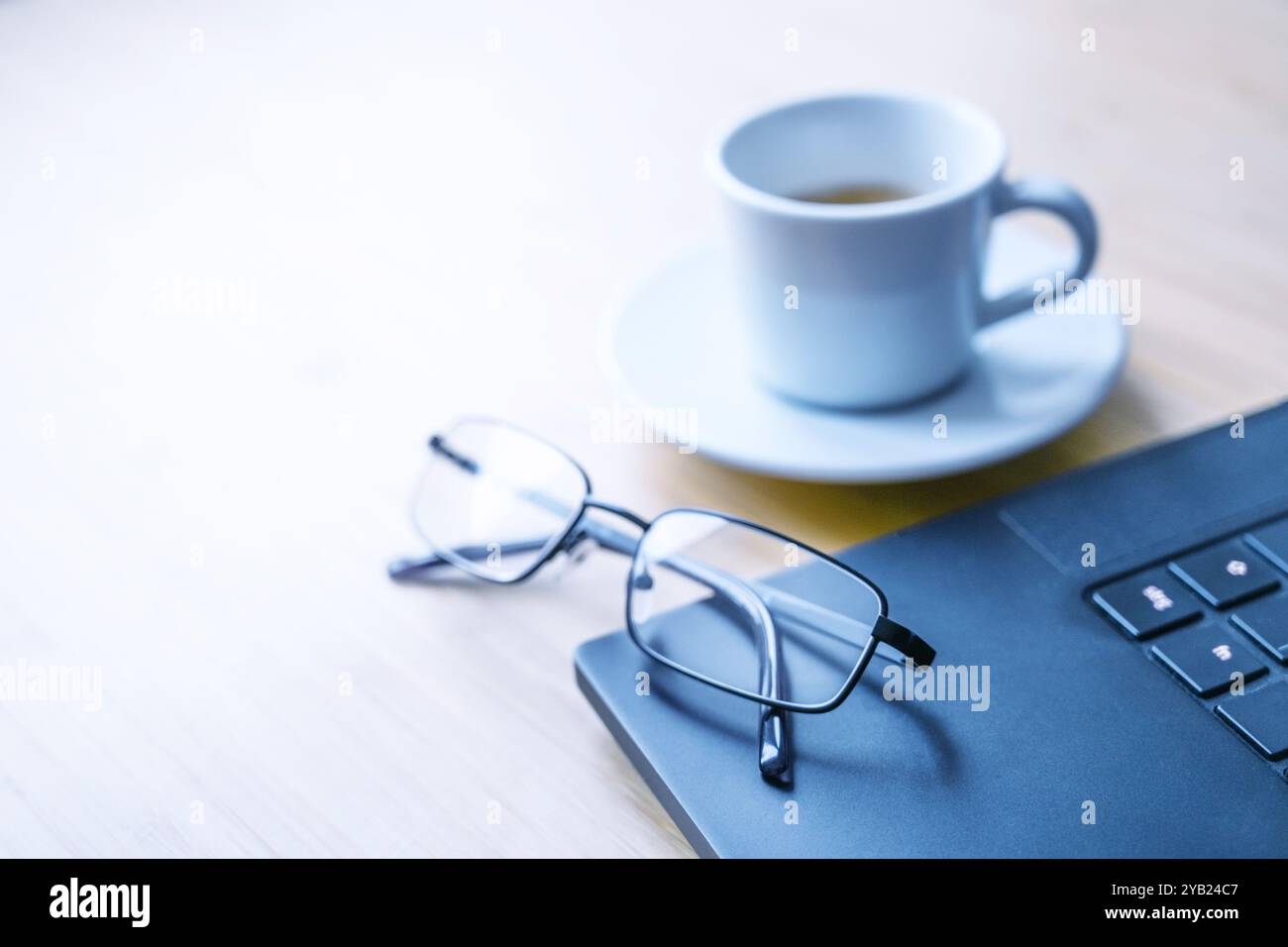 Parte di un computer portatile nero, bicchieri e una tazza di caffè su una scrivania di legno in un ufficio, concetto di lavoro, studio, scrittura o giornalismo, spazio di copia, sel Foto Stock