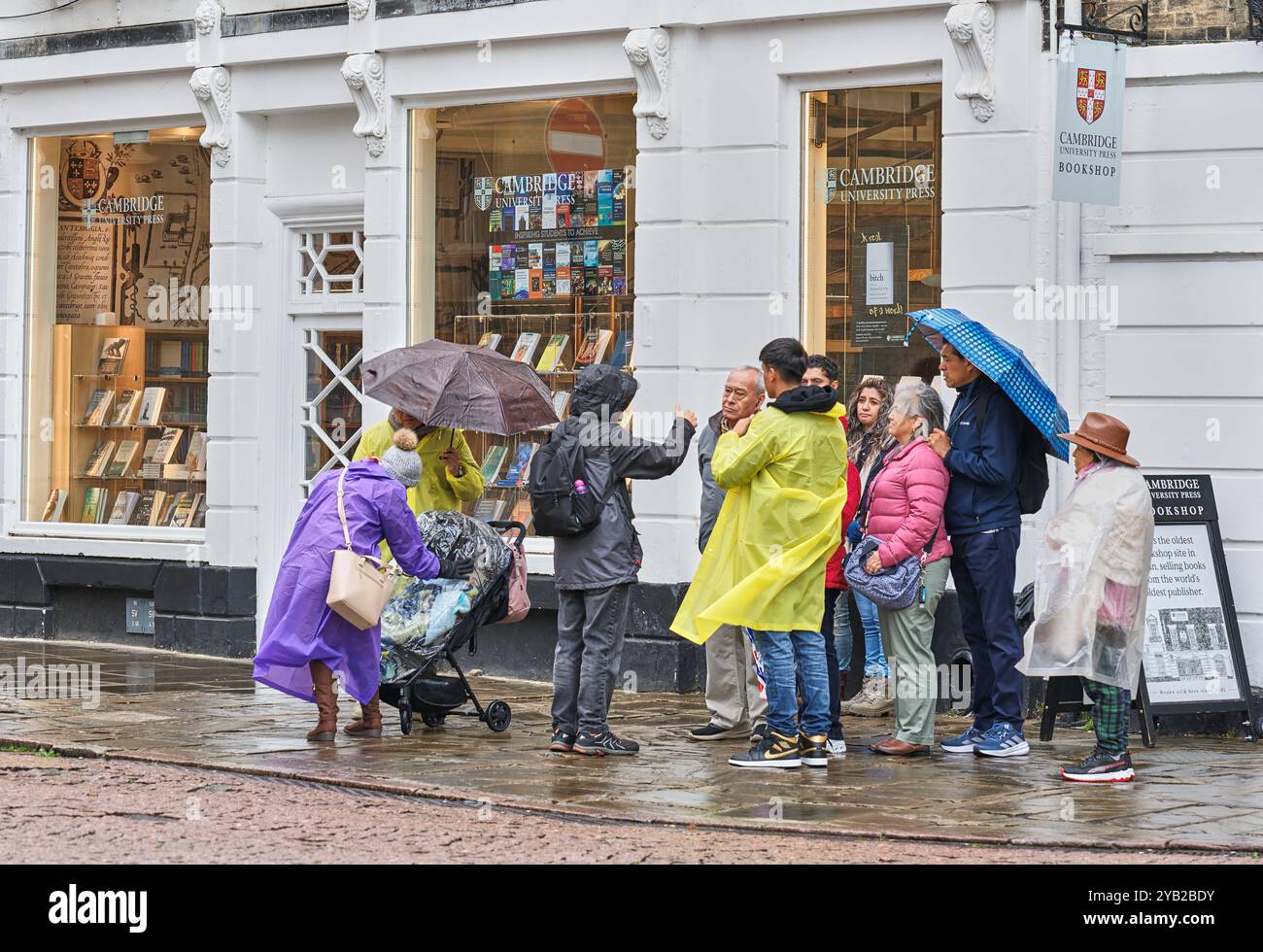 Un gruppo di turisti con guida fuori dalla libreria Cambridge University Press a Cambridge, in Inghilterra, in una giornata di pioggia. Foto Stock