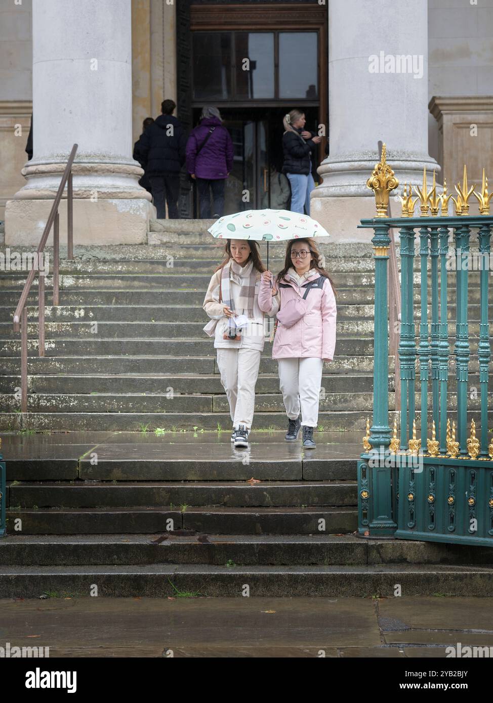 Un paio di giovani turisti con un ombrello lasciano il museo dell'Università Fitzwilliam a Cambridge, in Inghilterra, in una giornata di pioggia. Foto Stock