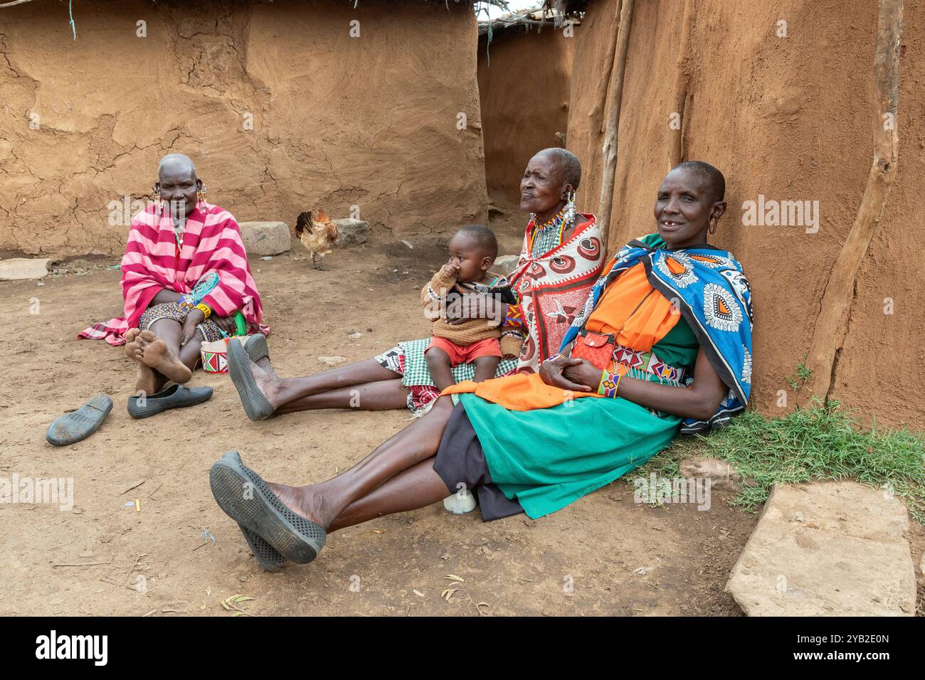 Gruppo di donne Masai che indossano costumi tradizionali, sedute e chiacchierate fuori da una casa tradizionale fatta di sterco e fango di mucca, villaggio Masai, Foto Stock