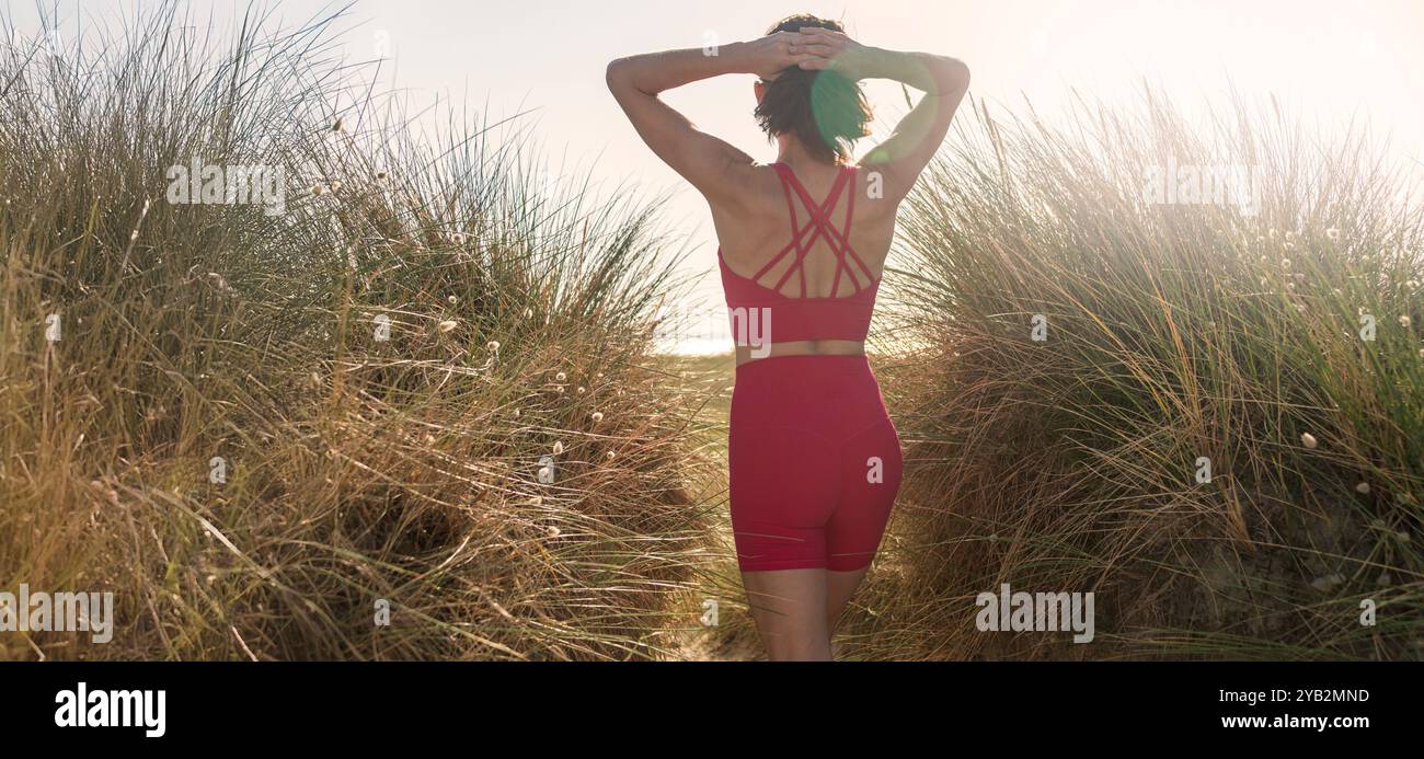 Vista posteriore di una donna in spiaggia che cammina attraverso le dune di sabbia Foto Stock