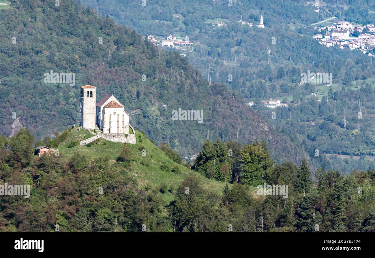 Paesaggio montano autunnale in cornice; Pieve di San Floriano su una collina: Illegio dai colori caldi sotto un cielo limpido. Foto Stock