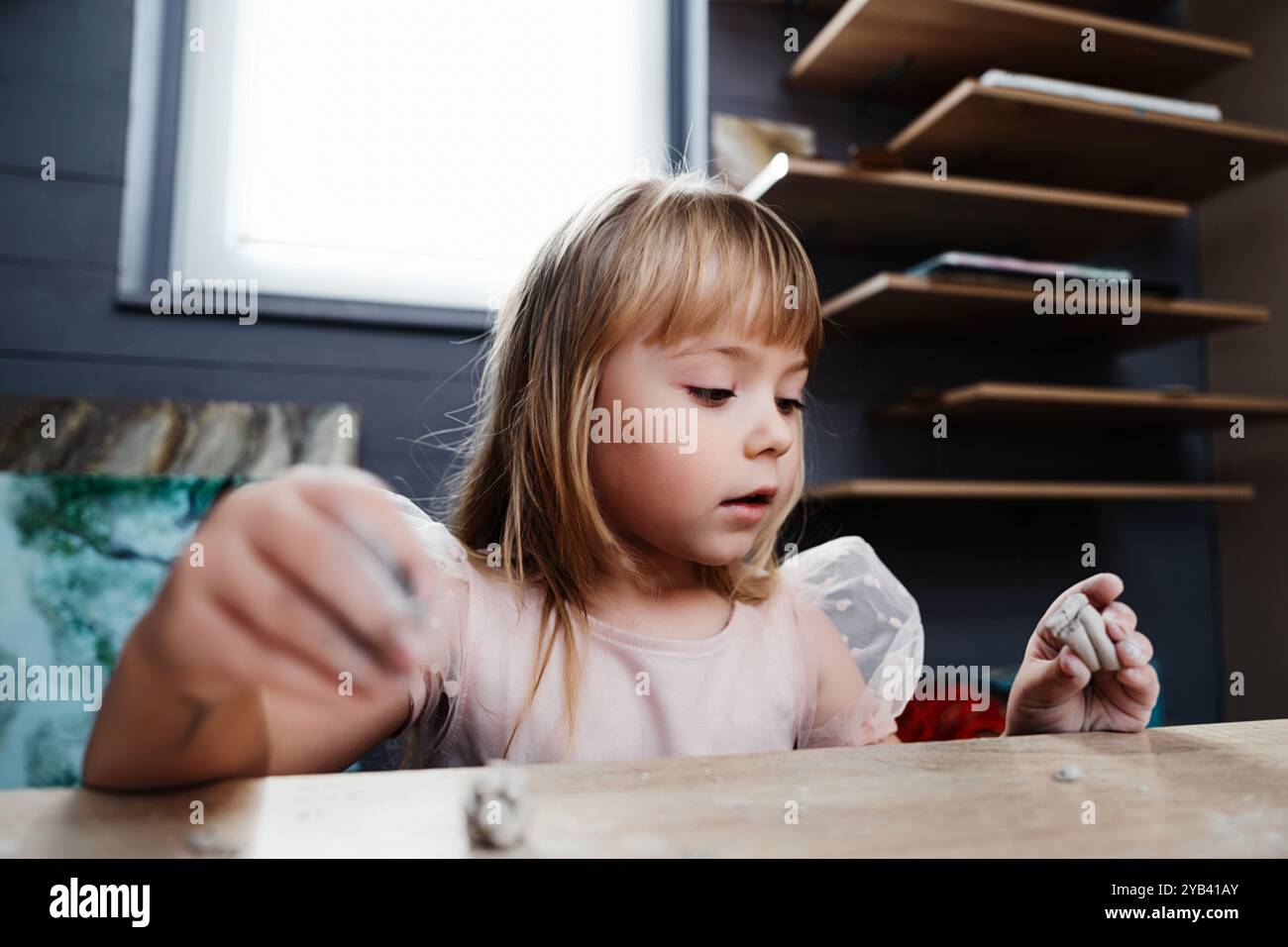Ragazza impegnata nella modellazione creativa dell'argilla in interni in un ambiente accogliente Foto Stock