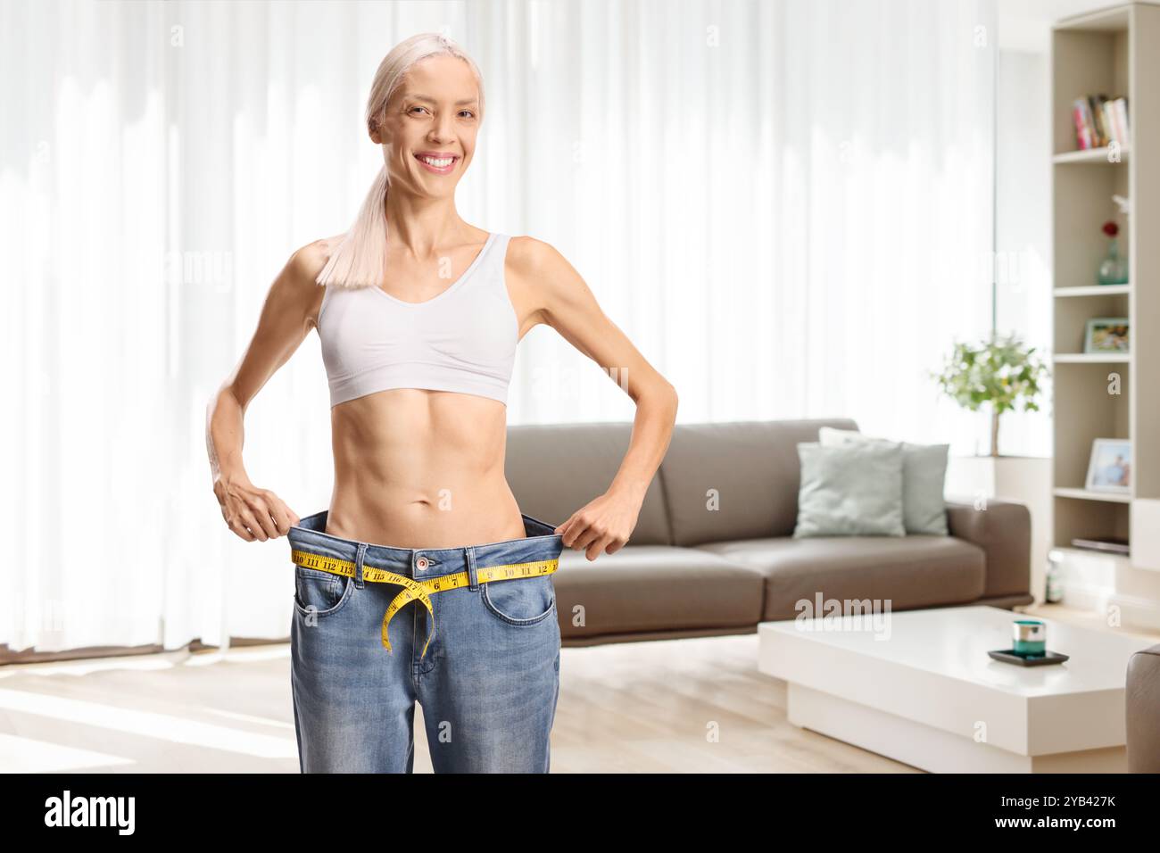 Donna sottile e felice in un paio di jeans grandi e top in crescita in salotto Foto Stock