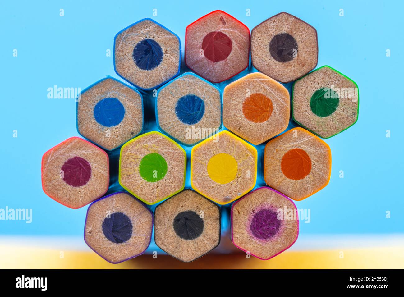 Questa immagine mostra una vista ravvicinata delle estremità posteriori di un fascio di matite colorate disposte in un motivo esagonale su uno sfondo blu. Foto Stock
