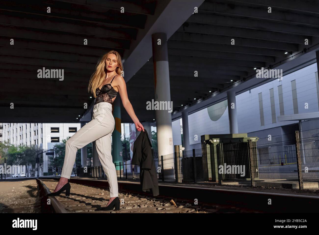 Uno splendido modello biondo si posa su binari ferroviari al tramonto Foto Stock