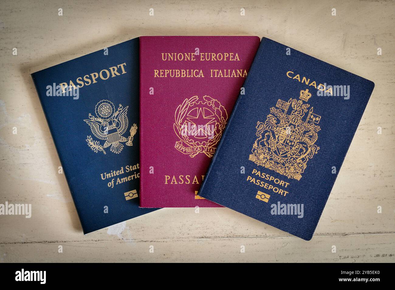 Tre passaporti, provenienti dal Canada, dall'Italia e dagli Stati Uniti d'America, sono stesi su un tavolo di legno bianco Foto Stock