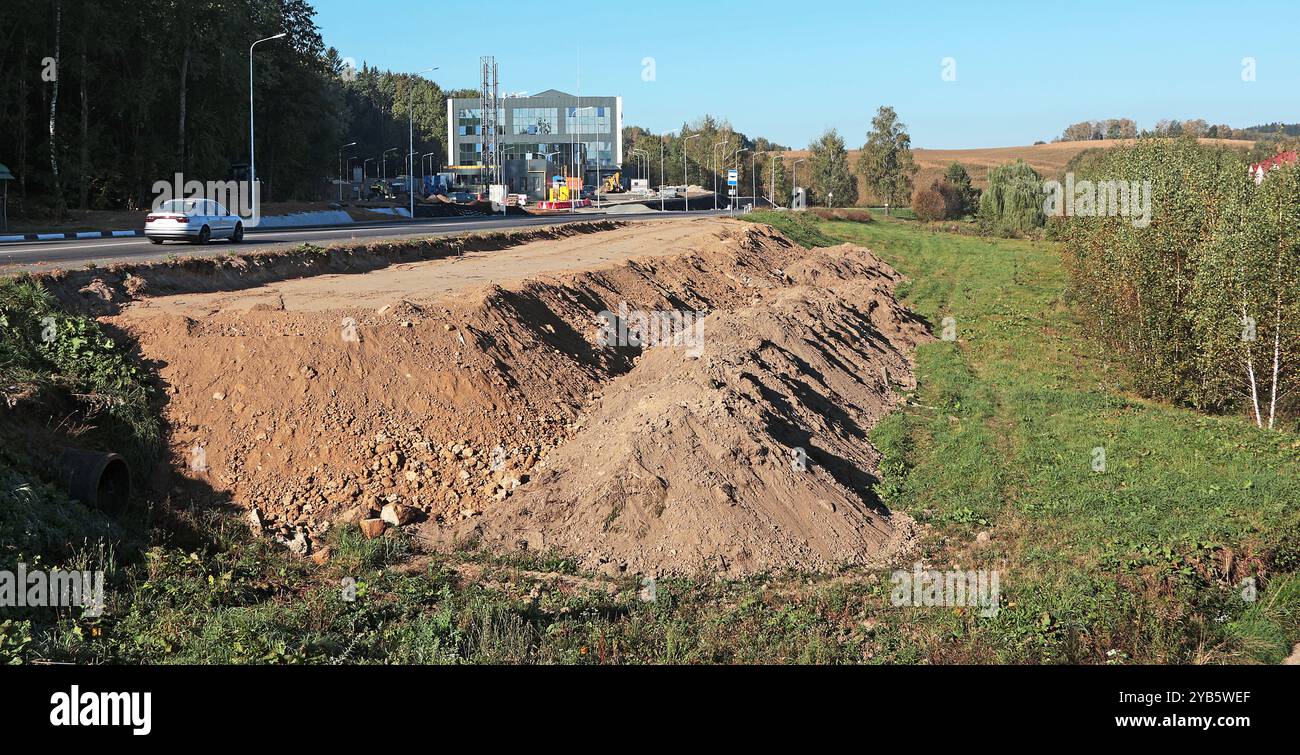 Terreno di livellamento per la costruzione della fermata dell'autobus. Mucchi di terra in cantiere vicino alla strada. Foto Stock