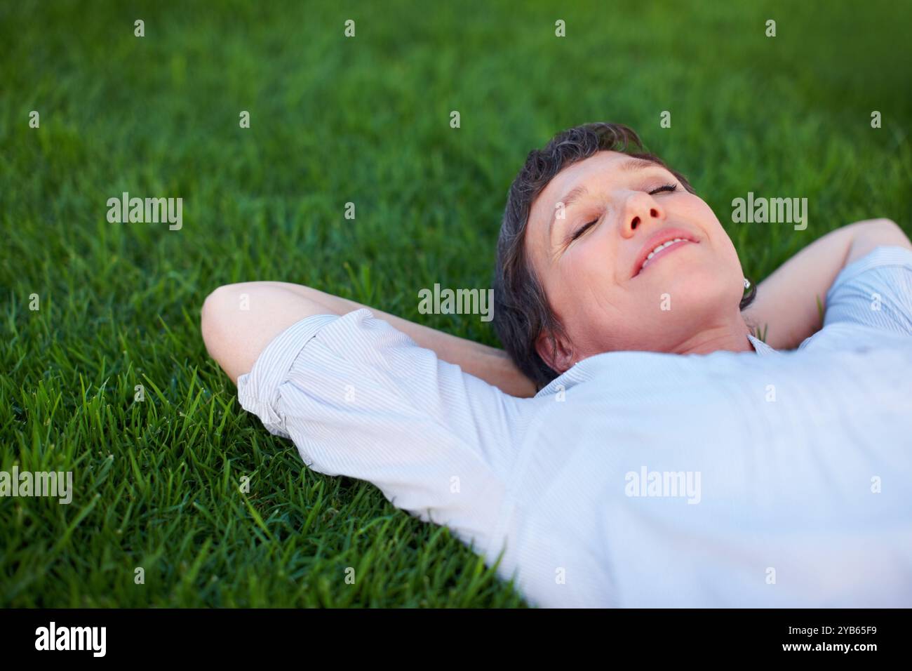 Donna, pace e relax su erba spazio per il comfort, zen e salute mentale positiva. Riposante, persona matura e sorriso nel parco naturale per i viaggi estivi Foto Stock