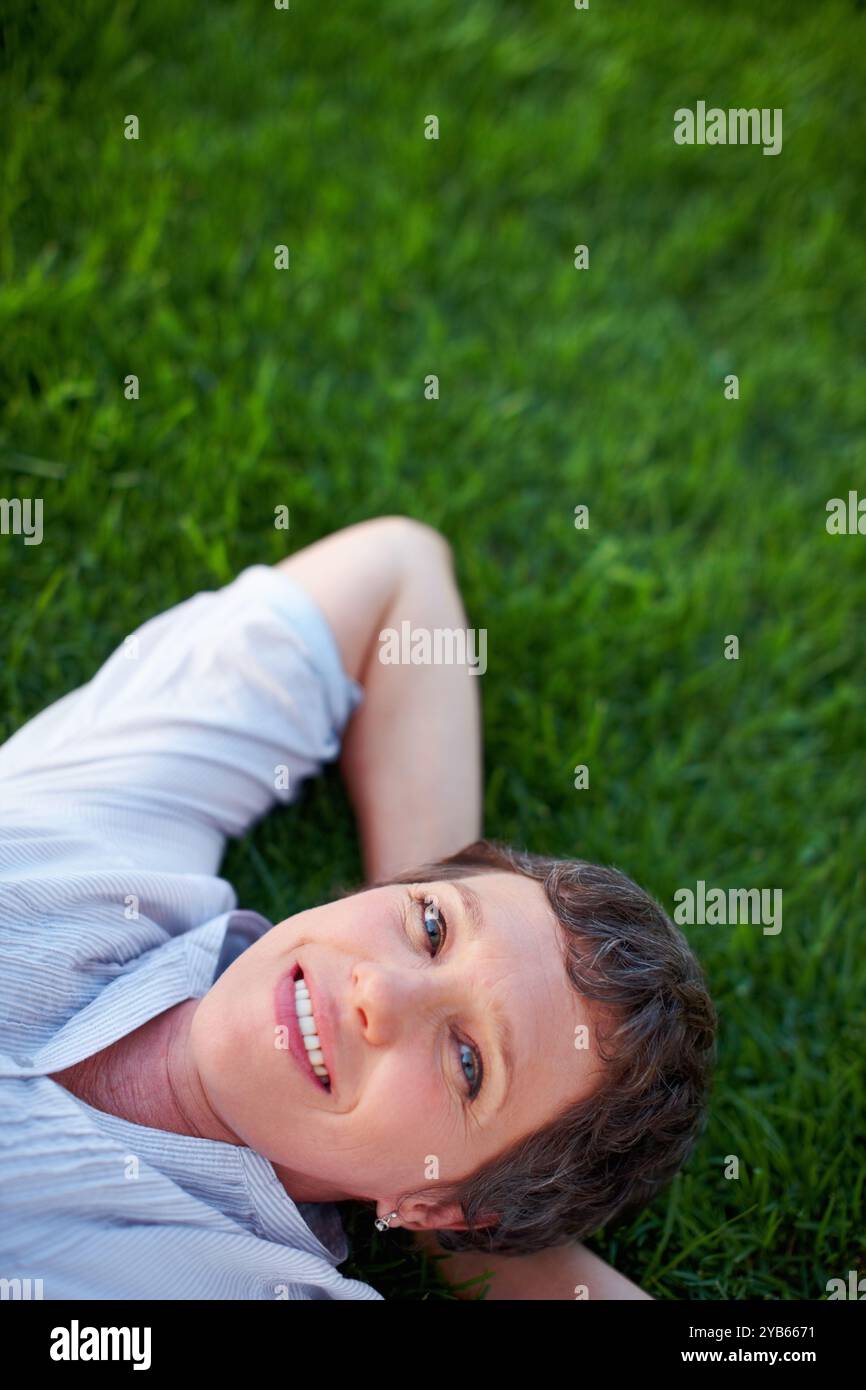Donna, ritratto e felice su erba spazio per relax, pace e salute mentale positiva. Una persona calma, matura e sorrisi nel parco naturale per il comfort estivo Foto Stock