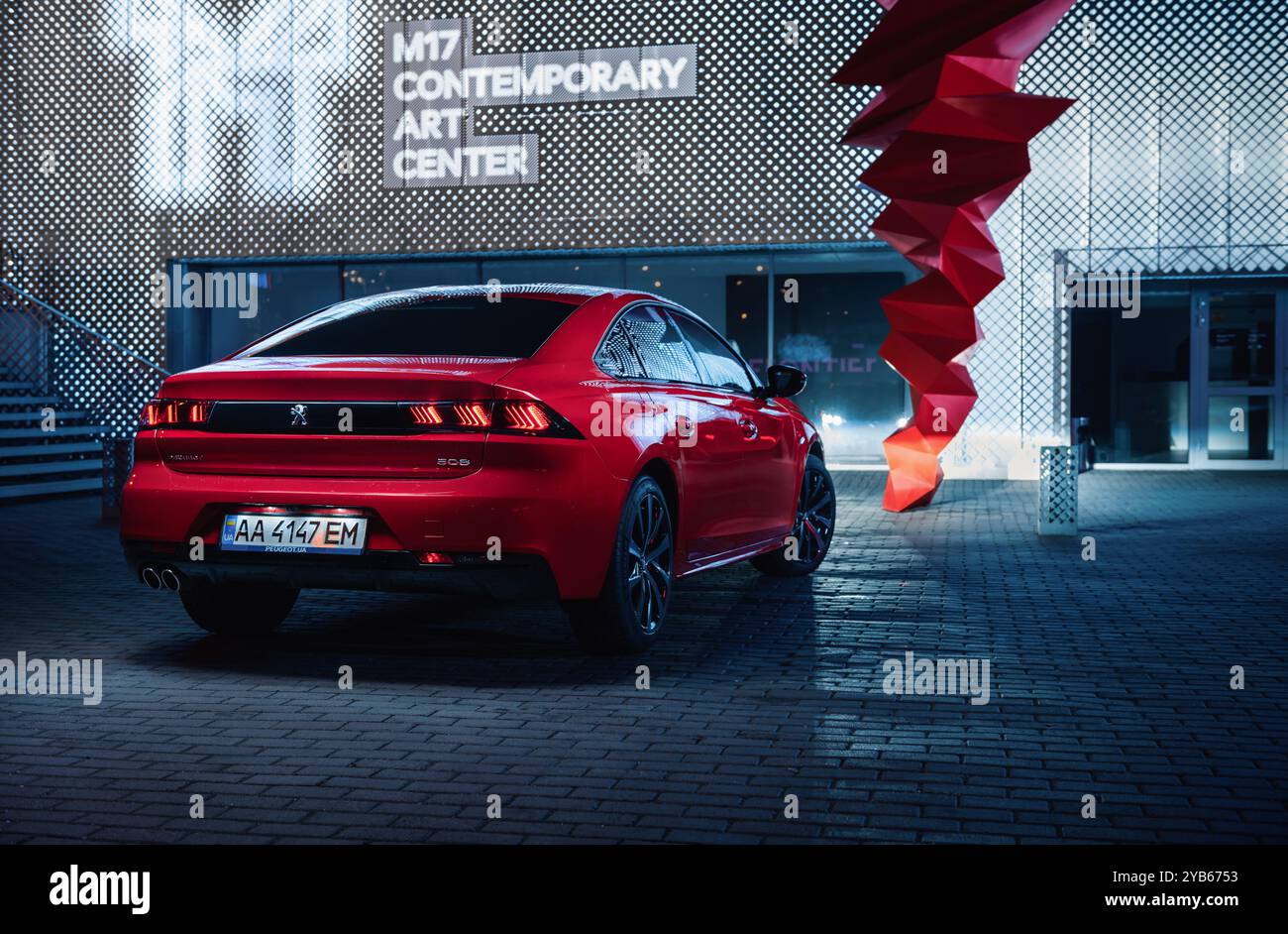 Red Peugeot 508 nella città notturna. Vista posteriore di tre quarti dell'elegante berlina nelle fredde notti, edificio illuminato sullo sfondo. Foto Stock