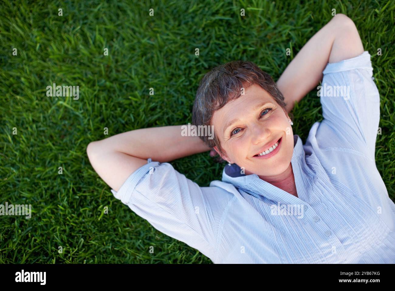 Donna felice, ritratto e relax su spazio erba per comfort, pace e salute mentale positiva. In alto, persona matura e sorriso nel parco naturale per l'estate Foto Stock