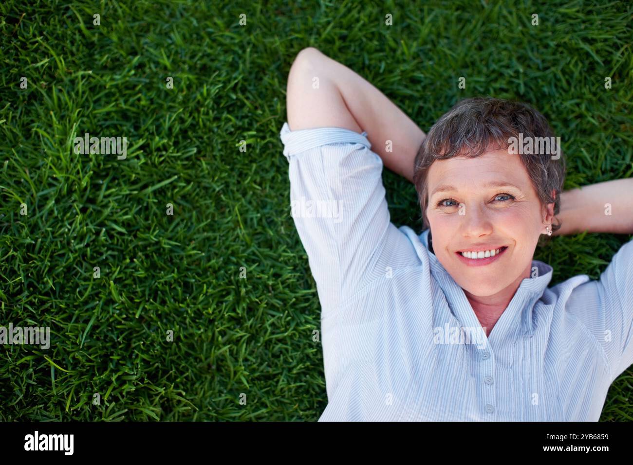 Donna, ritratto e sorriso sull'erba spazio per relax, pace e salute mentale positiva. Sopra, persona matura e felice nel parco naturale per l'estate, viaggiare Foto Stock
