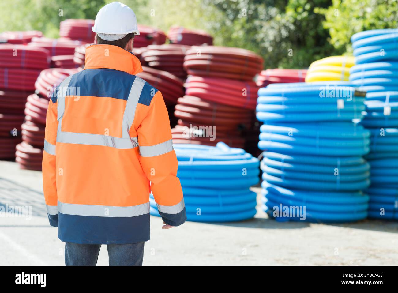 operaio edile che cammina verso una pila di tubi protettivi Foto Stock