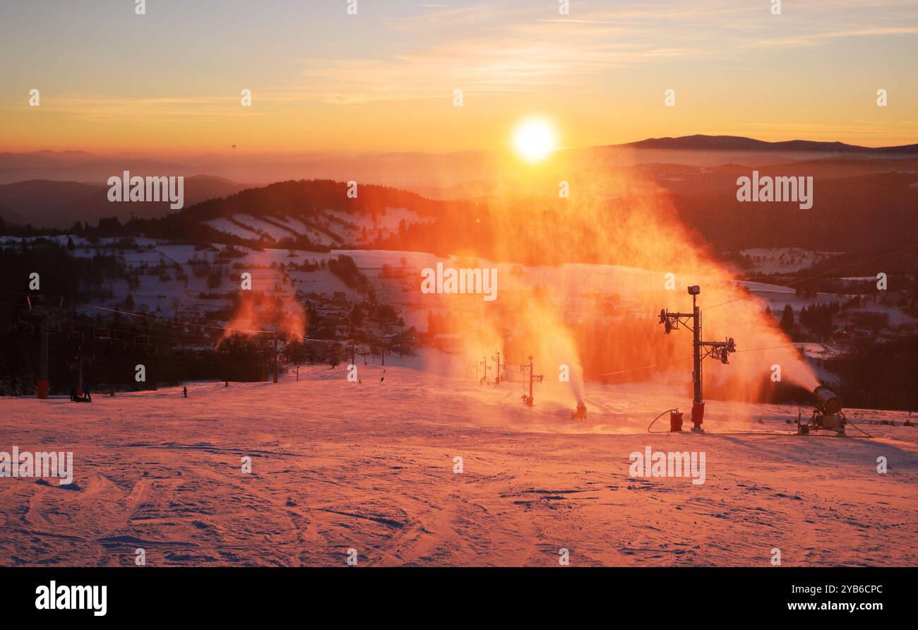 Snowmaker che produce neve in una stazione sciistica. Snowjet in luce laterale e con sfondo scuro al tramonto Foto Stock