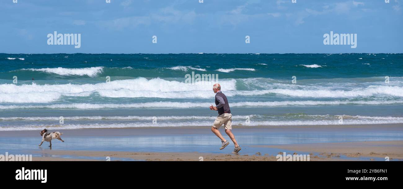 Un'immagine panoramica di un uomo che corre dietro al suo cane sulla GT Great Western Beach a Newquay in Cornovaglia nel Regno Unito. Foto Stock