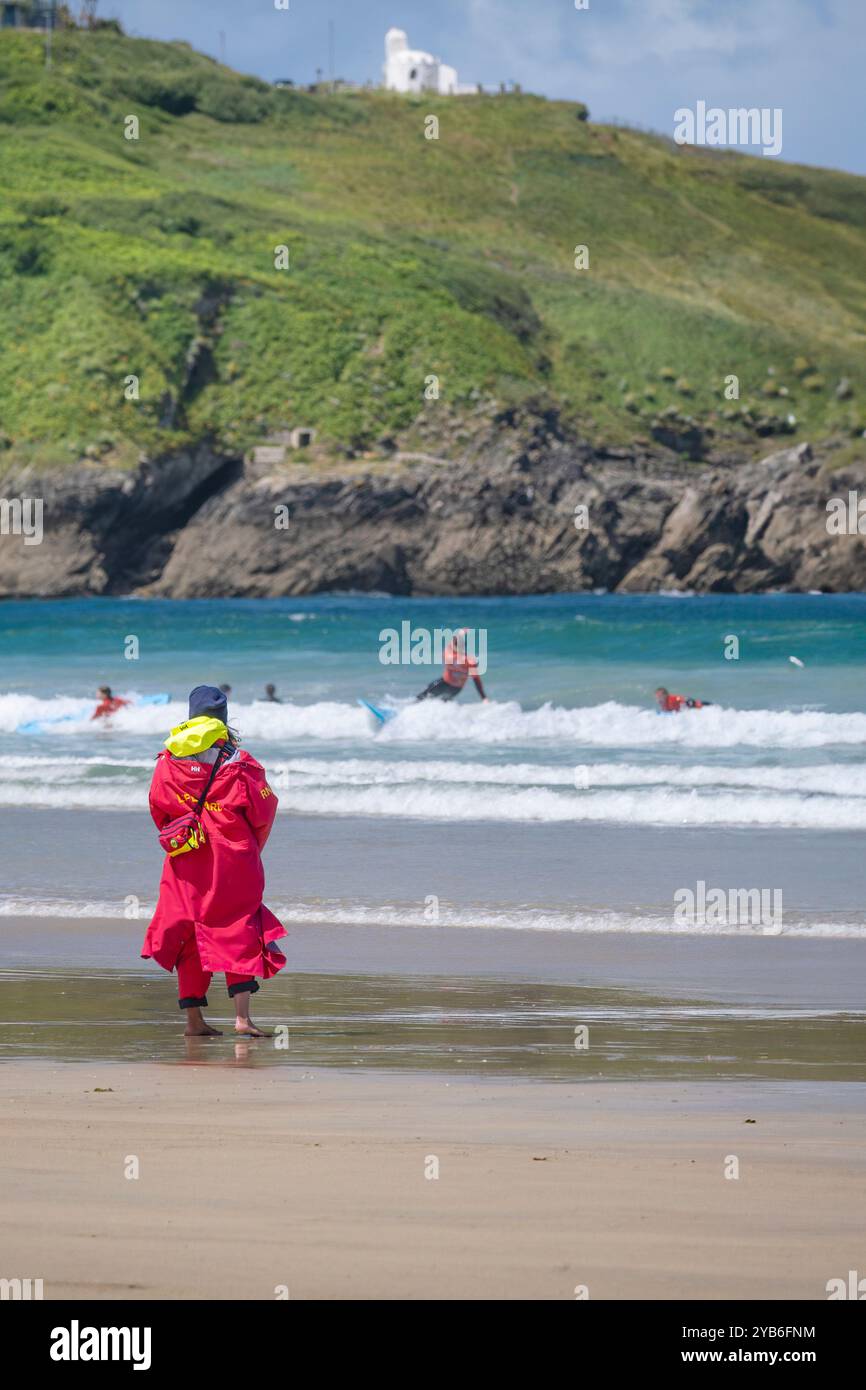 Un bagnino della Royal National Lifeboat Institution della RNLI, in servizio sulla riva, osservando i surfisti principianti che tengono una lezione di surf in mare a Towan Foto Stock