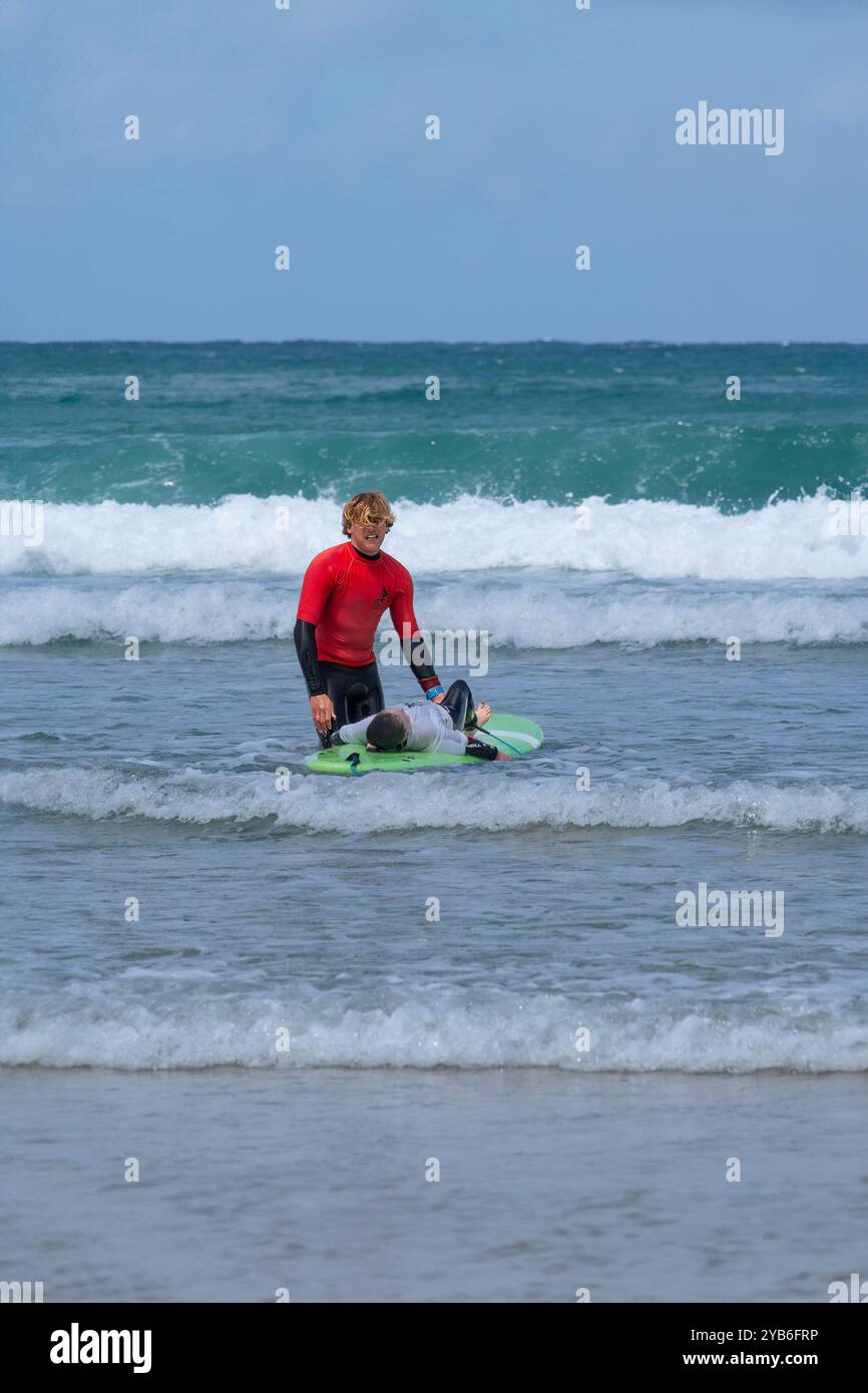 Un giovane surfista principiante con un istruttore di surf che impara a fare surf a Towan Beach a Newquay in Cornovaglia nel Regno Unito. Foto Stock