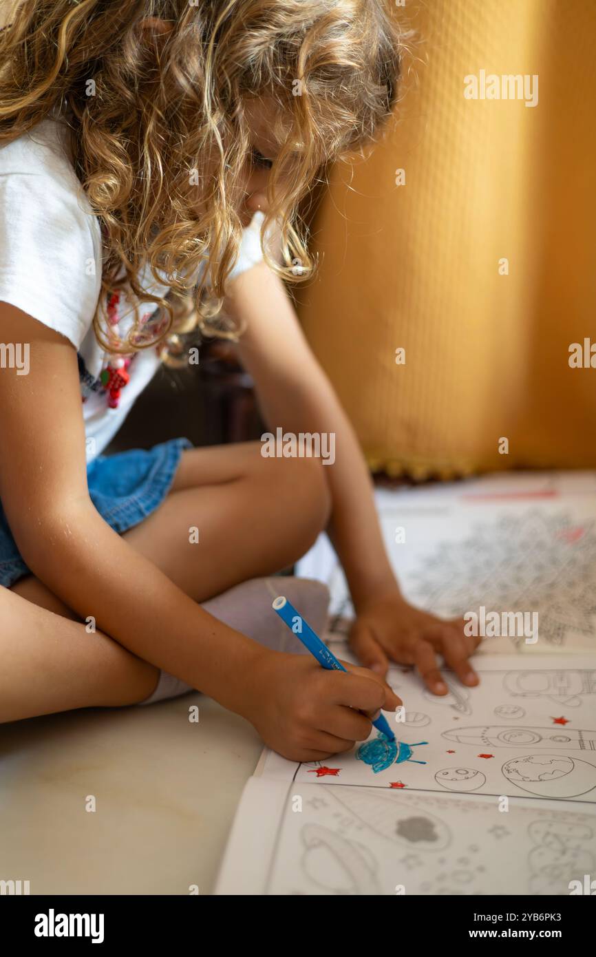 Un bambino che si concentra sulla colorazione di una pagina a tema spaziale in un libro, mostrando concentrazione e abilità creative. Foto Stock