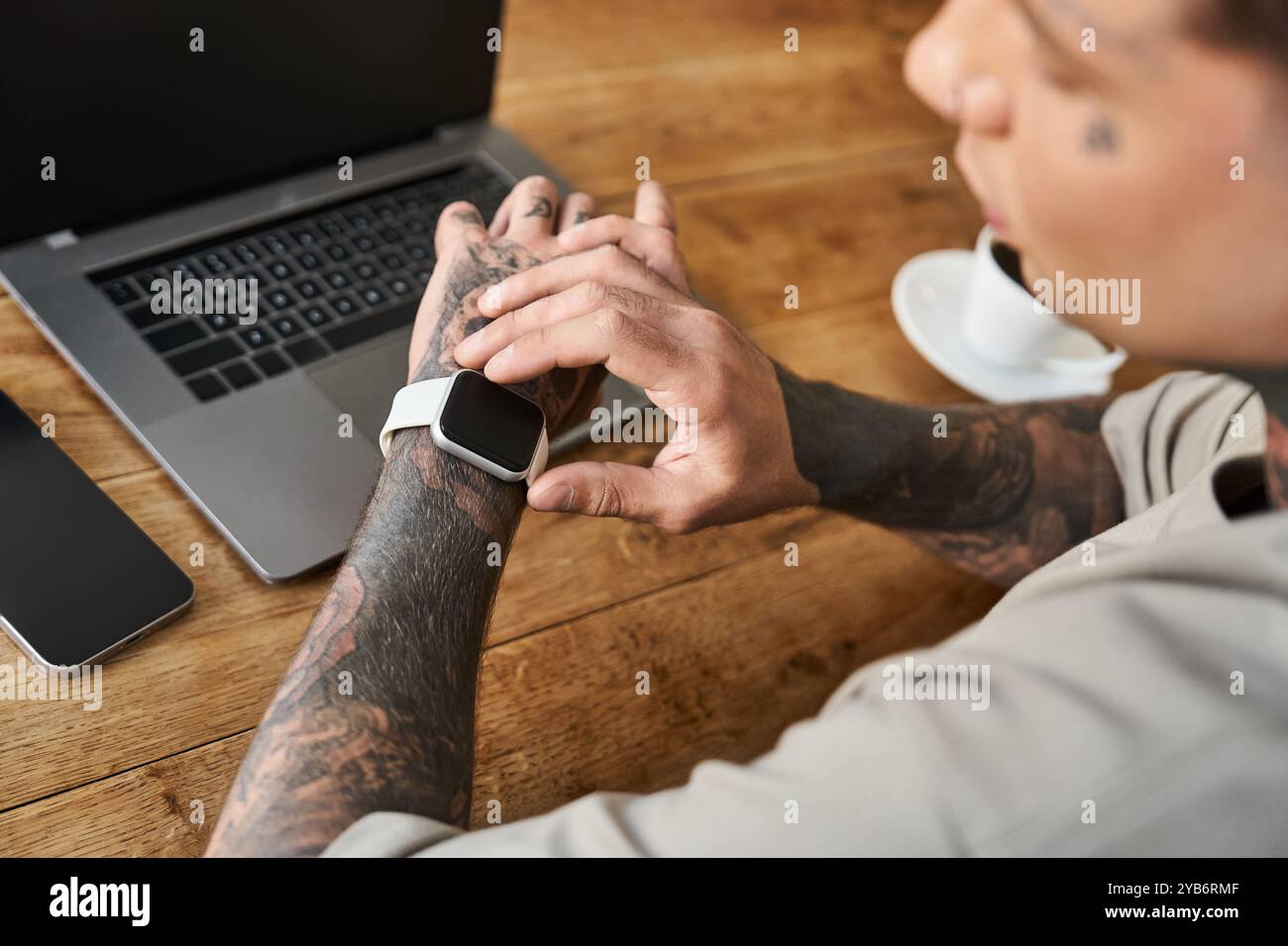Un giovane uomo elegante controlla attentamente il suo smartwatch seduto a una scrivania. Foto Stock