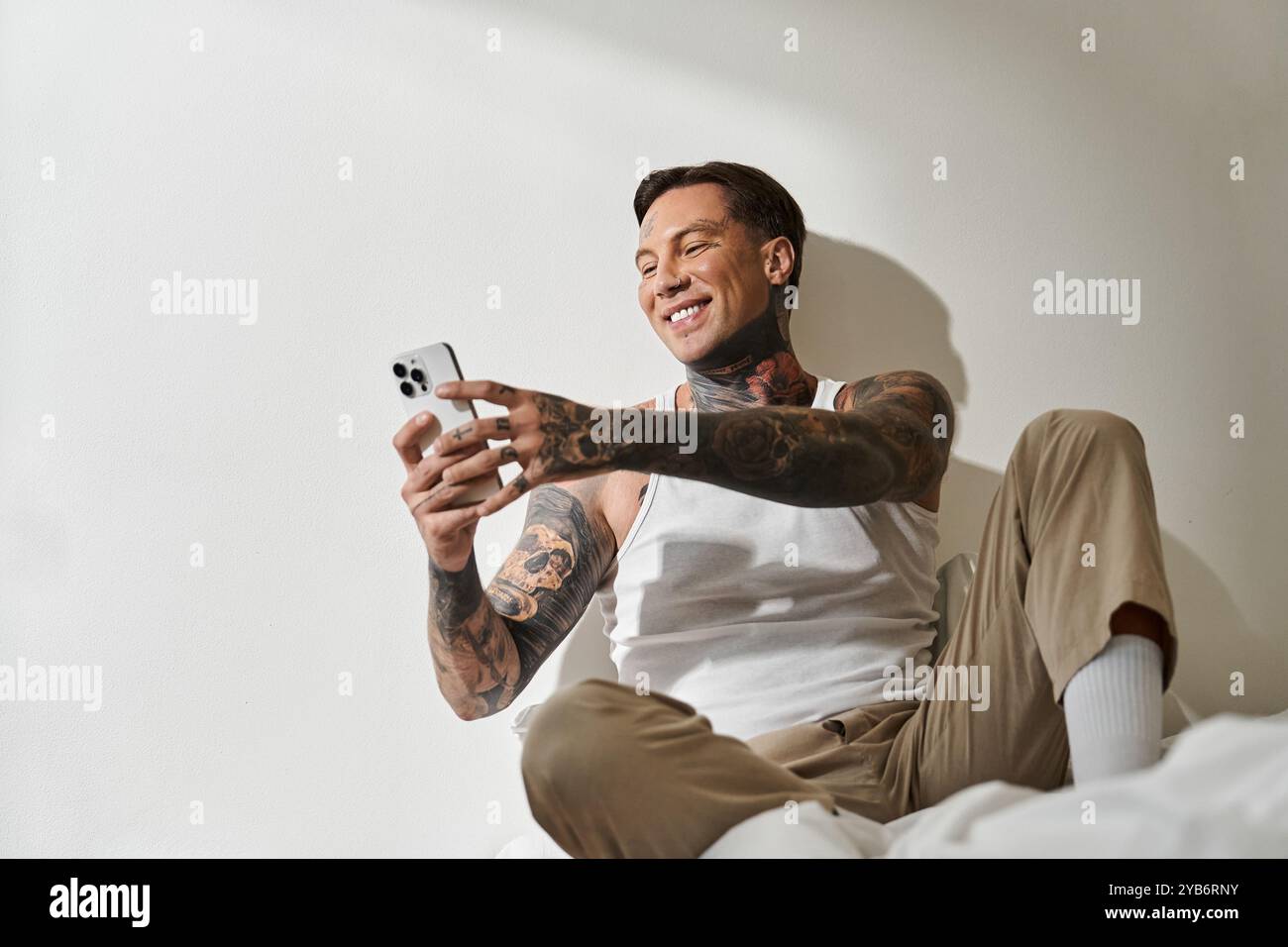 Un giovane uomo elegante si rilassa a casa, sorridendo calorosamente mentre interagisce con il suo smartphone. Foto Stock