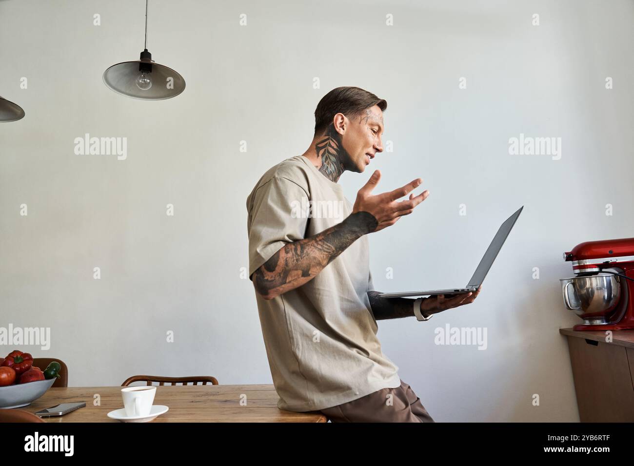 Un giovane a casa che discute con passione sul suo portatile mentre è seduto casualmente. Foto Stock