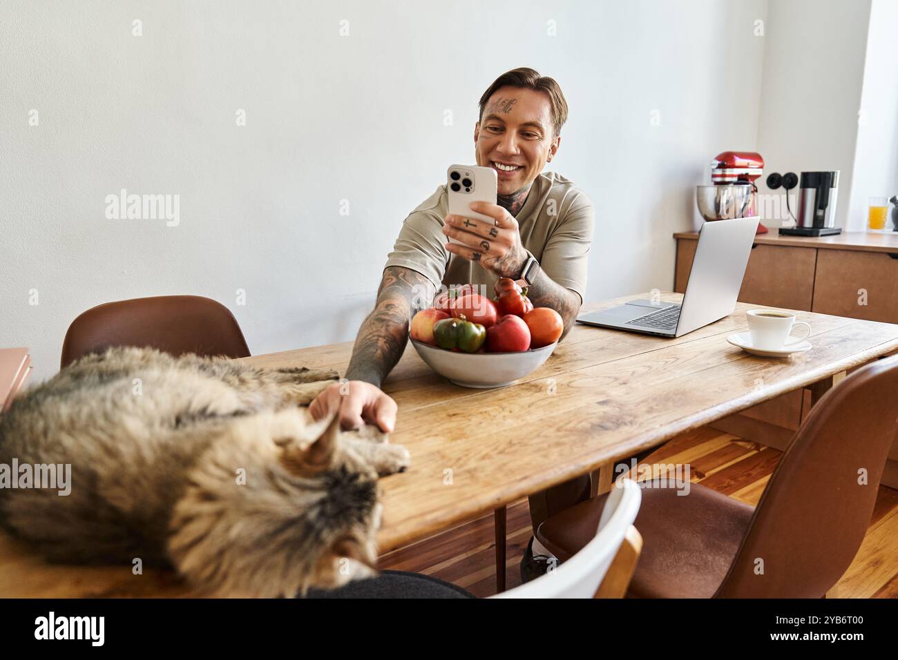 Un giovane sorride mentre interagisce con il suo gatto mentre è circondato da frutta fresca. Foto Stock