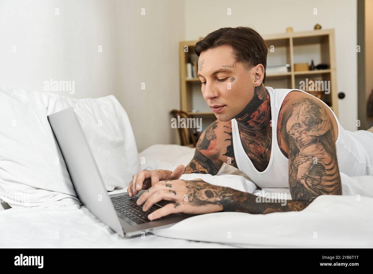 Un giovane con i tatuaggi si impegna con il suo portatile mentre si rilassa a letto a casa. Foto Stock