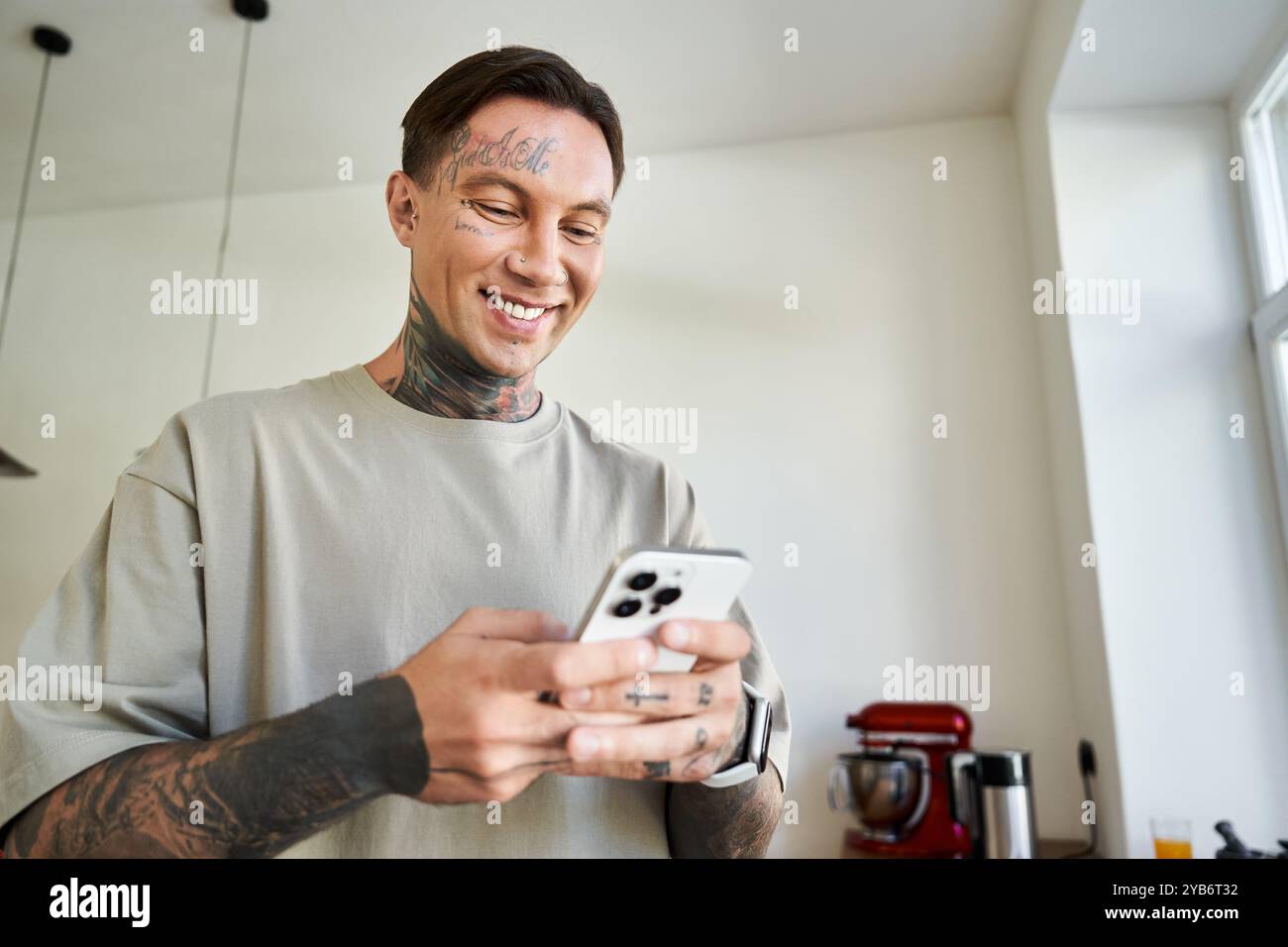 Un uomo giovane e attraente si rilassa a casa, sorridendo mentre naviga sul suo smartphone. Foto Stock