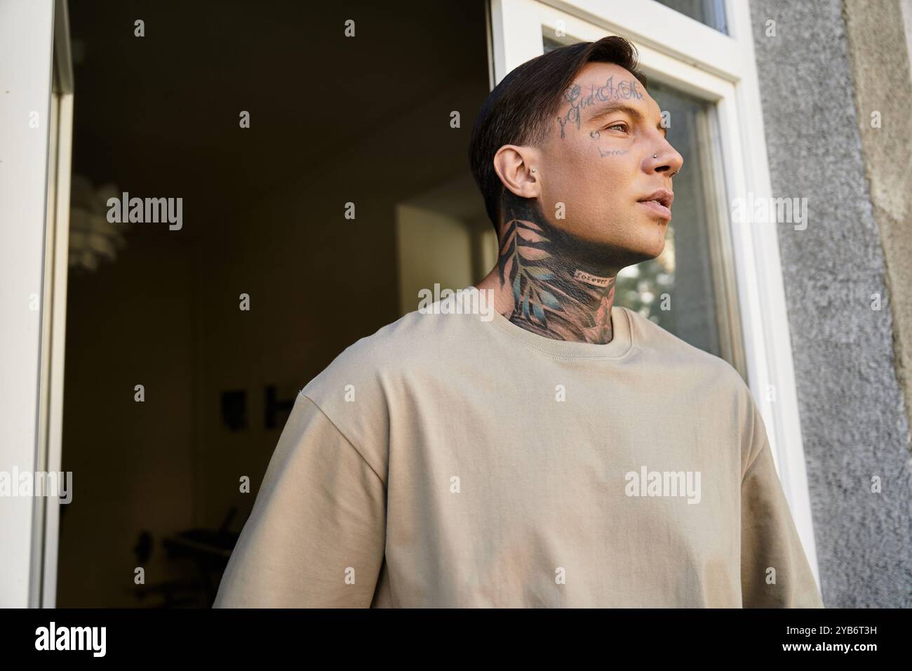 Davanti alla porta, un giovane tatuato contempla il mondo fuori da casa sua. Foto Stock