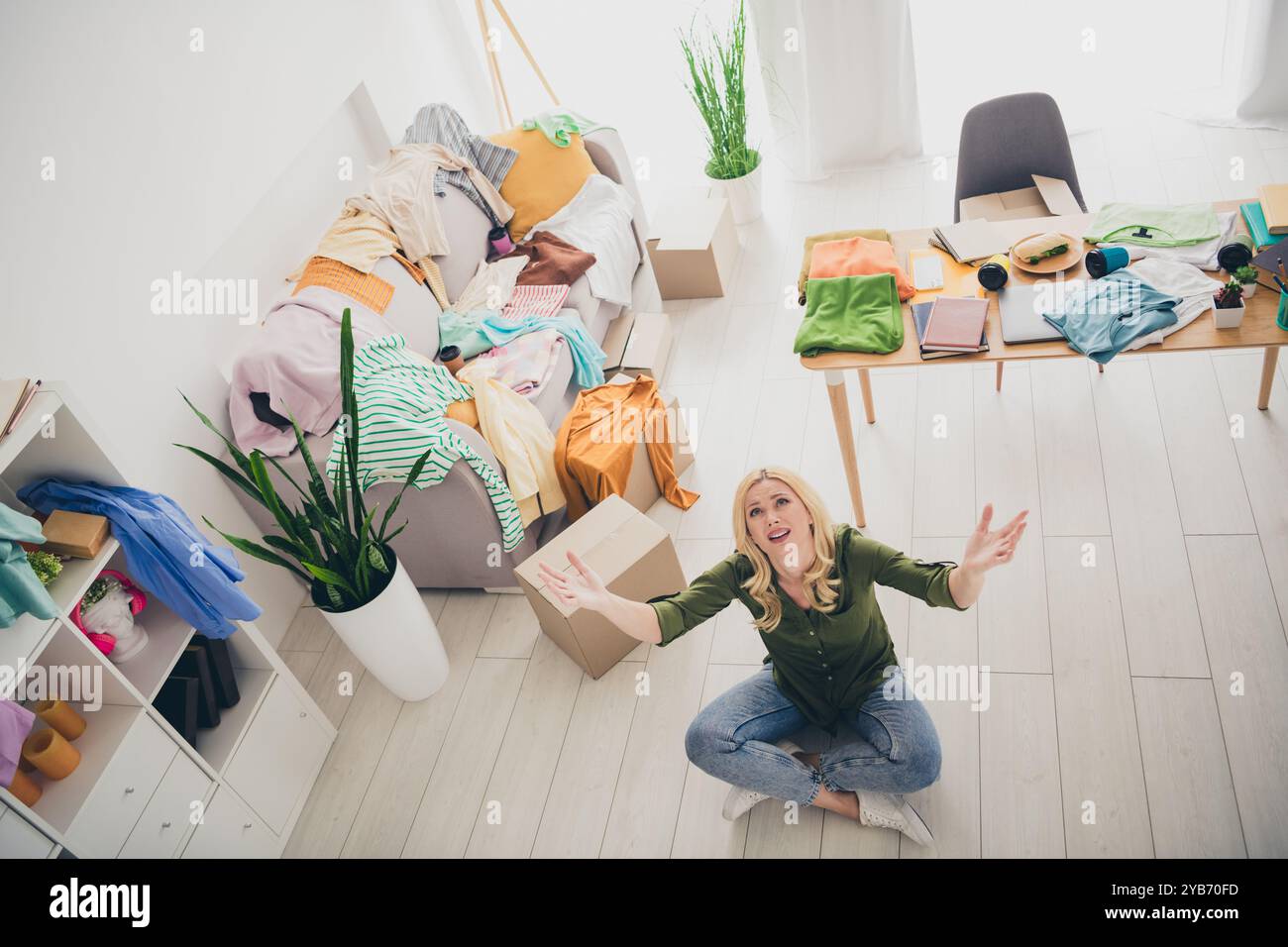 Foto di una giovane donna triste e turbata chiedere aiuto per spostare un nuovo appartamento, un mucchio di vestiti, un salotto in casa Foto Stock