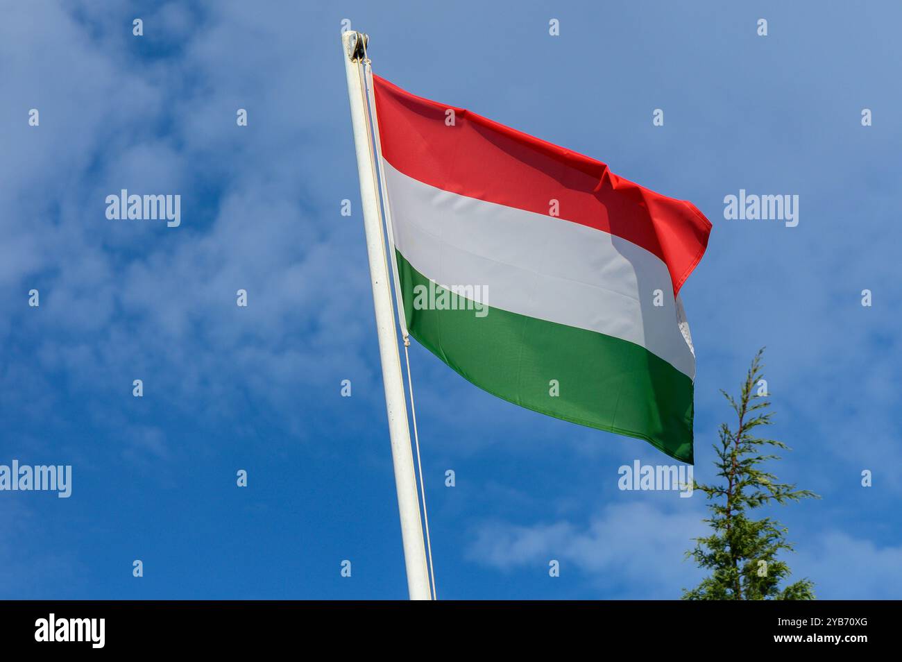 La bandiera ungherese, caratterizzata da strisce orizzontali rosse, bianche e verdi, fluttua nel vento sotto un cielo soleggiato adornato da nuvole di mogli. Foto Stock